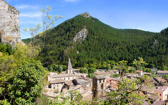 Village nestled in the Gorges du Verdon with a church spire and forested mountains.
