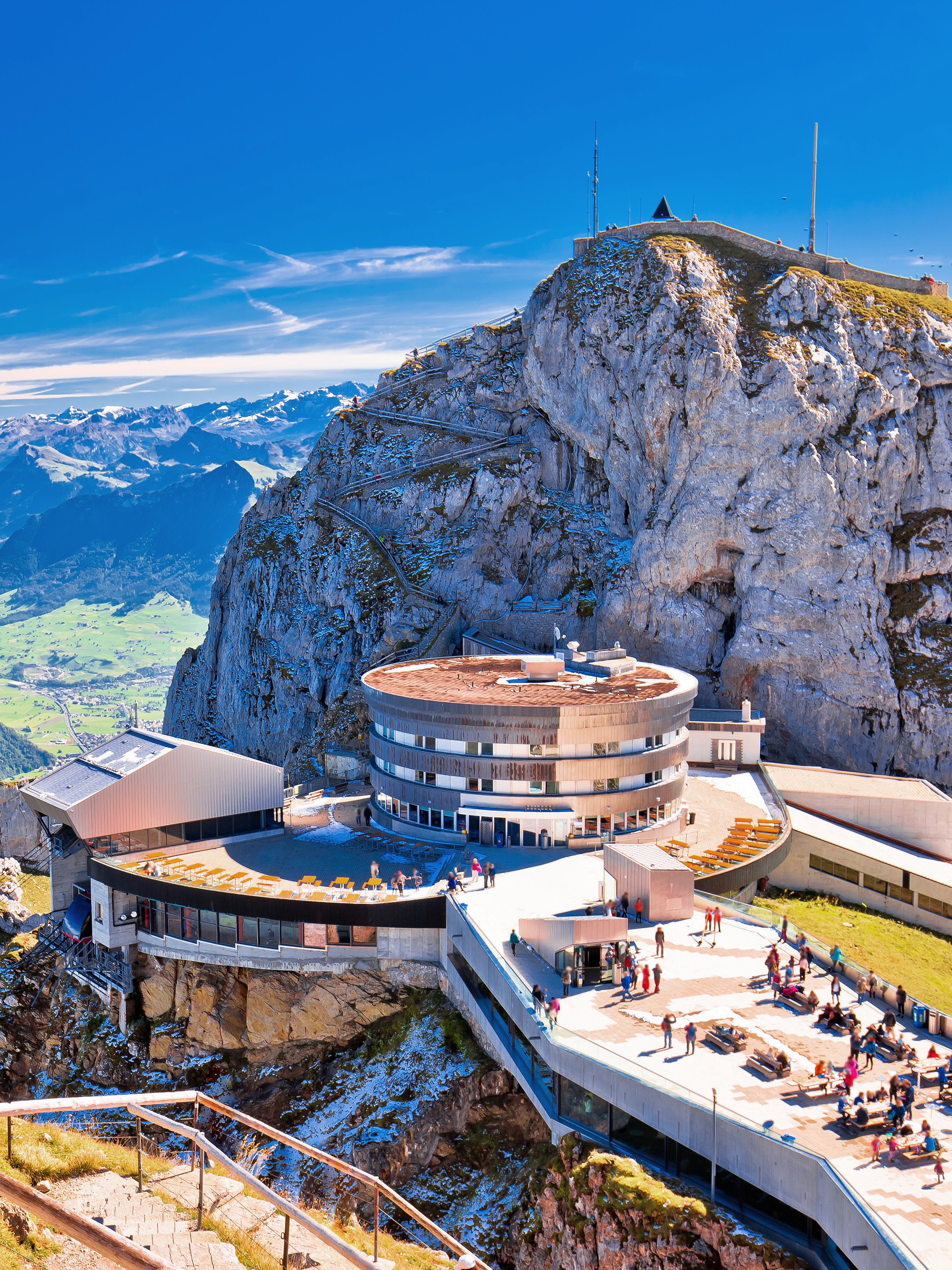 Mount Pilatus summit with visitors on terrace and panoramic views of Swiss Alps.