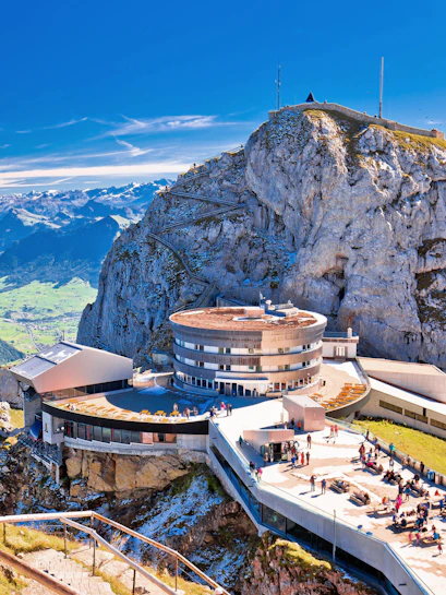 Mount Pilatus summit with visitors on terrace and panoramic views of Swiss Alps.