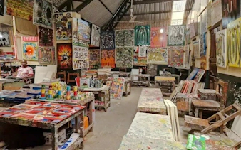 Art market with colorful paintings displayed in Dar es Salaam, part of the Masaki Walking Tuk-Tuk Fish Market & Sunset Tour.