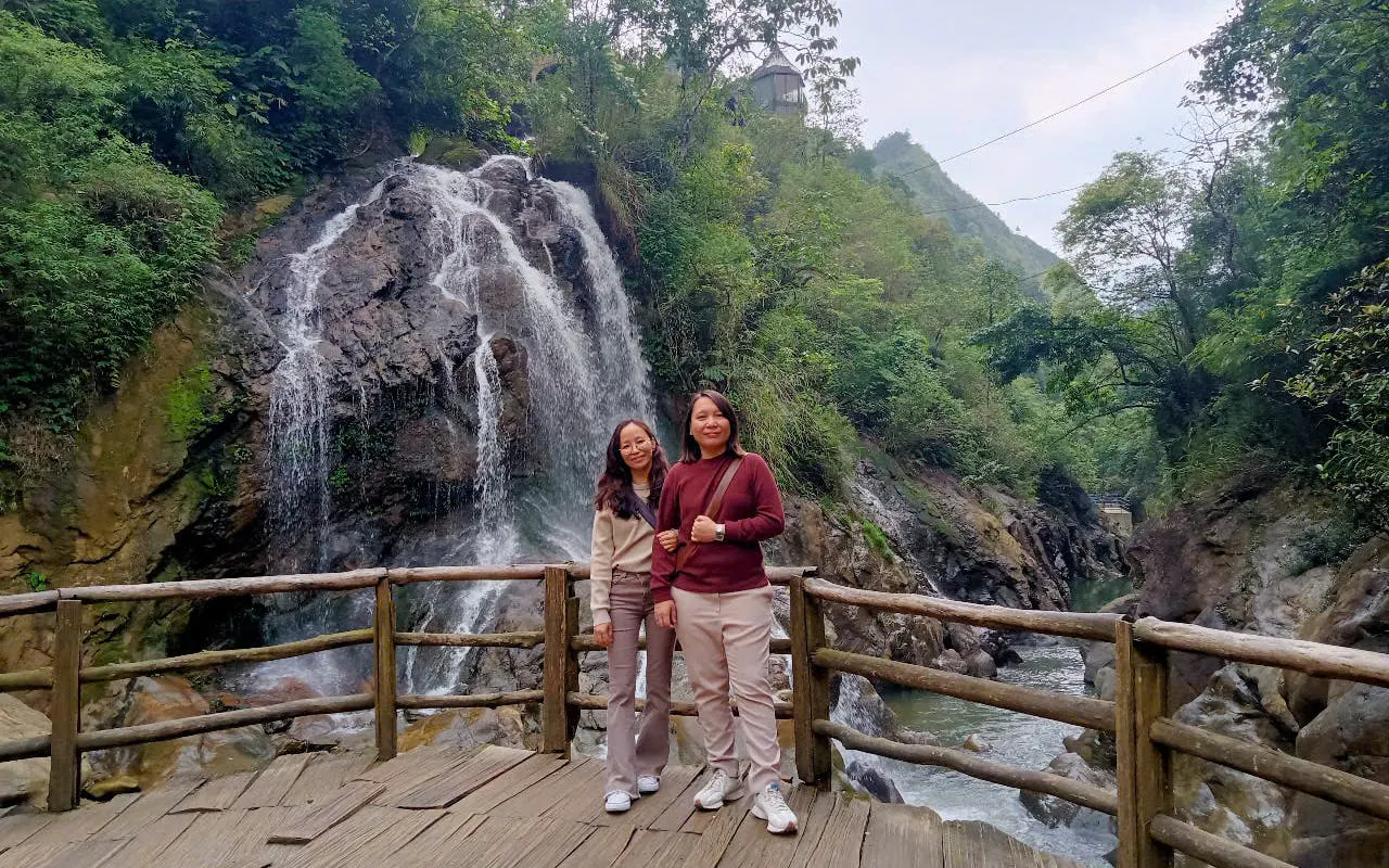 Two people standing on a wooden platform in front of a waterfall in Sapa, Vietnam.