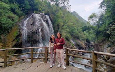 Two people standing on a wooden platform in front of a waterfall in Sapa, Vietnam.
