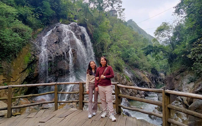 Two people standing on a wooden platform in front of a waterfall in Sapa, Vietnam.