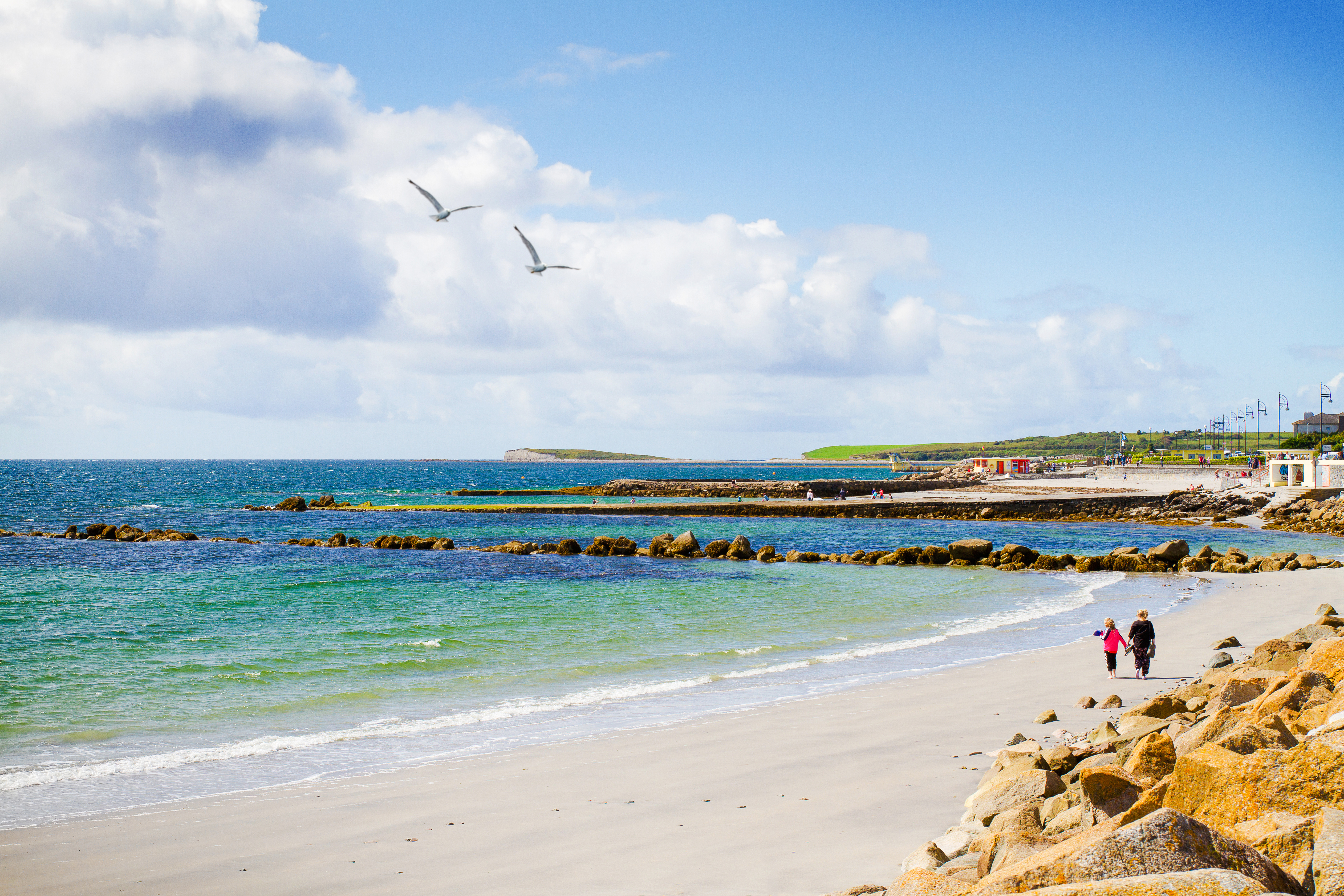 Sandy beach with people walking along Salthill Promenade, Galway, Ireland.