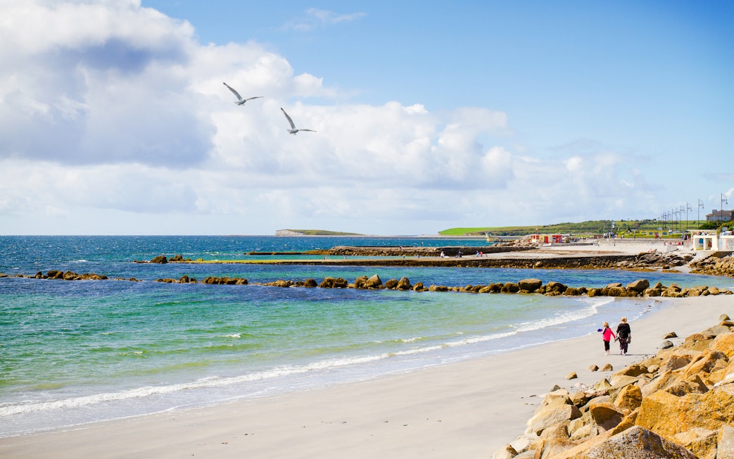 Sandy beach with people walking along Salthill Promenade, Galway, Ireland.
