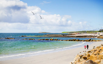 Sandy beach with people walking along Salthill Promenade, Galway, Ireland.