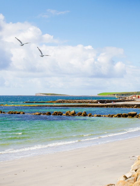 Sandy beach with people walking along Salthill Promenade, Galway, Ireland.