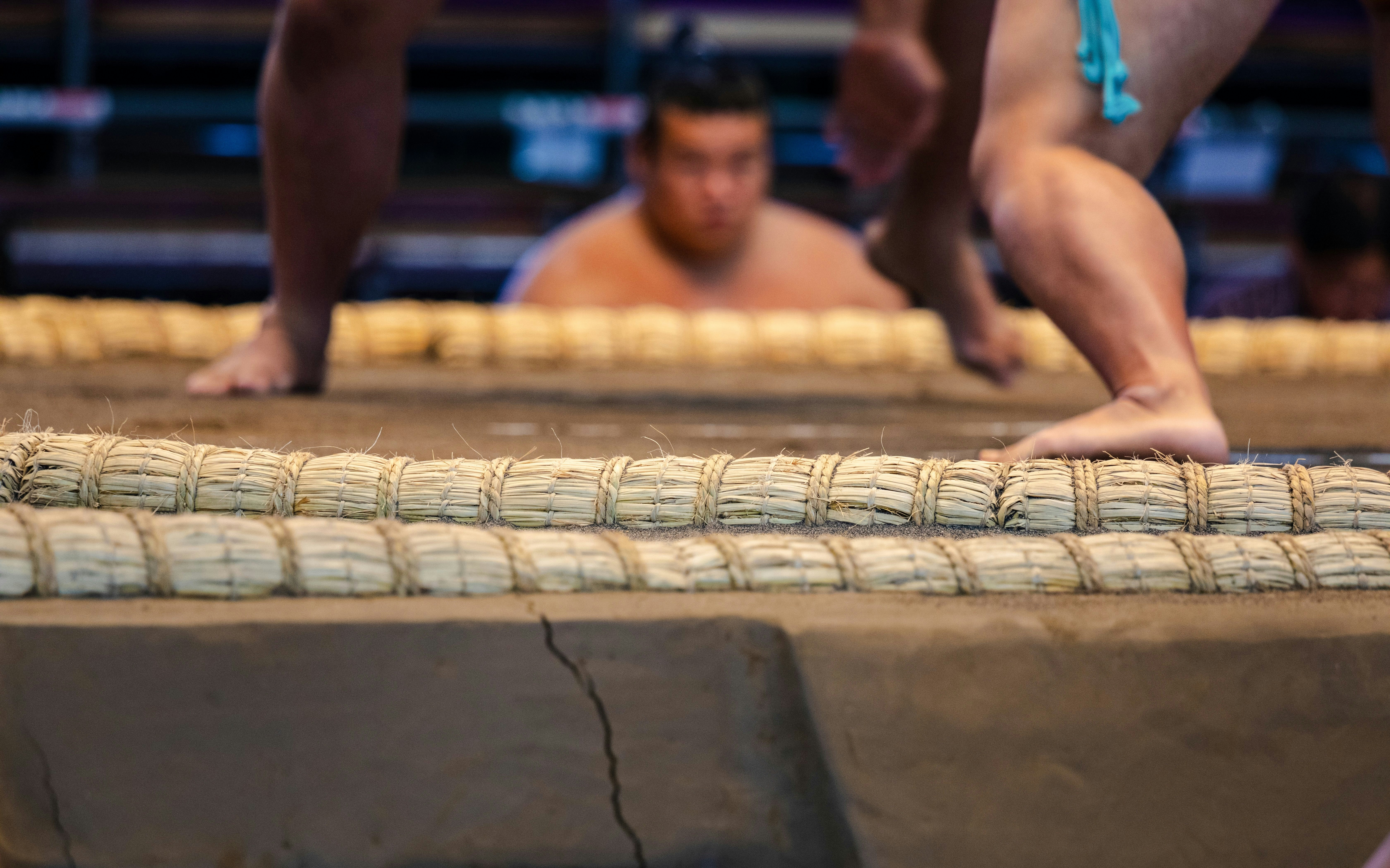 Sumo wrestlers in a clay ring, preparing for a match under bright lights.