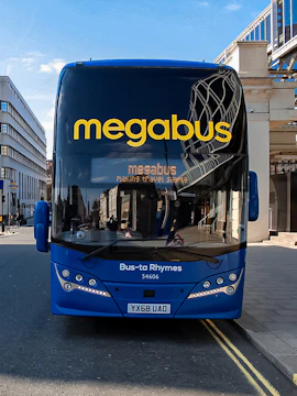 Megabus parked on a city street with modern buildings in the background.