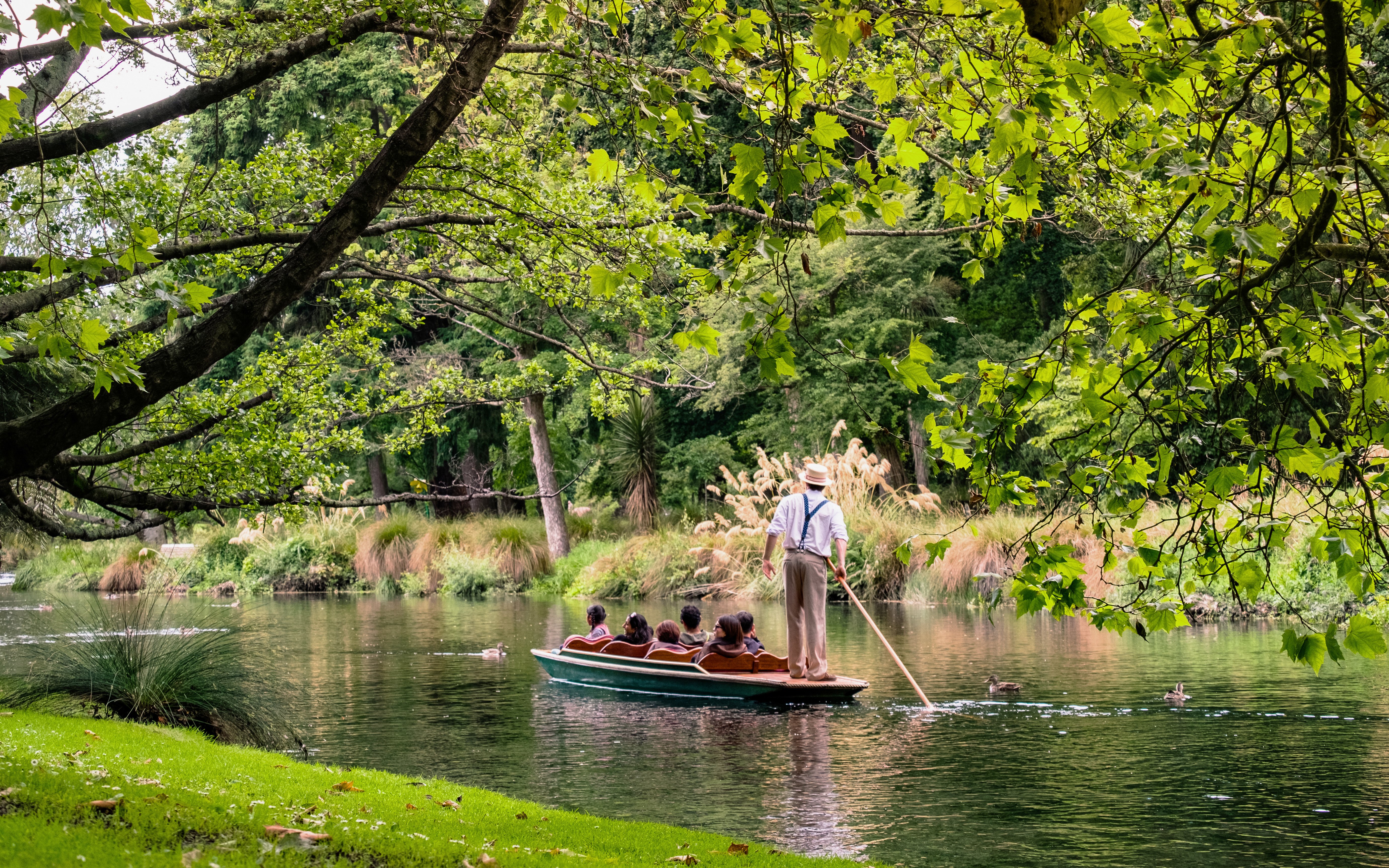 Punting ride on Avon River, Christchurch with guide and passengers amidst lush greenery.