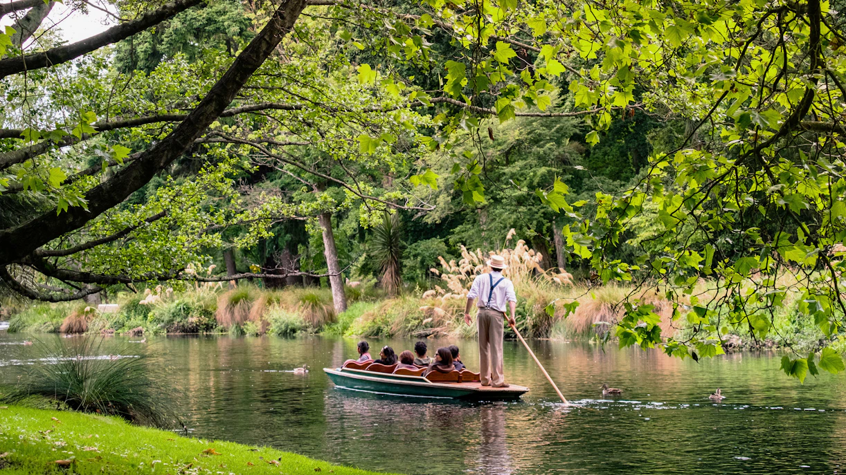 Punting ride on Avon River, Christchurch with guide and passengers amidst lush greenery.