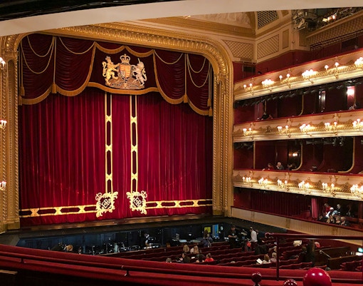 Interior of the Royal Opera House in London with red velvet curtains and ornate balconies.