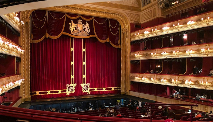 Interior of the Royal Opera House in London with red velvet curtains and ornate balconies.