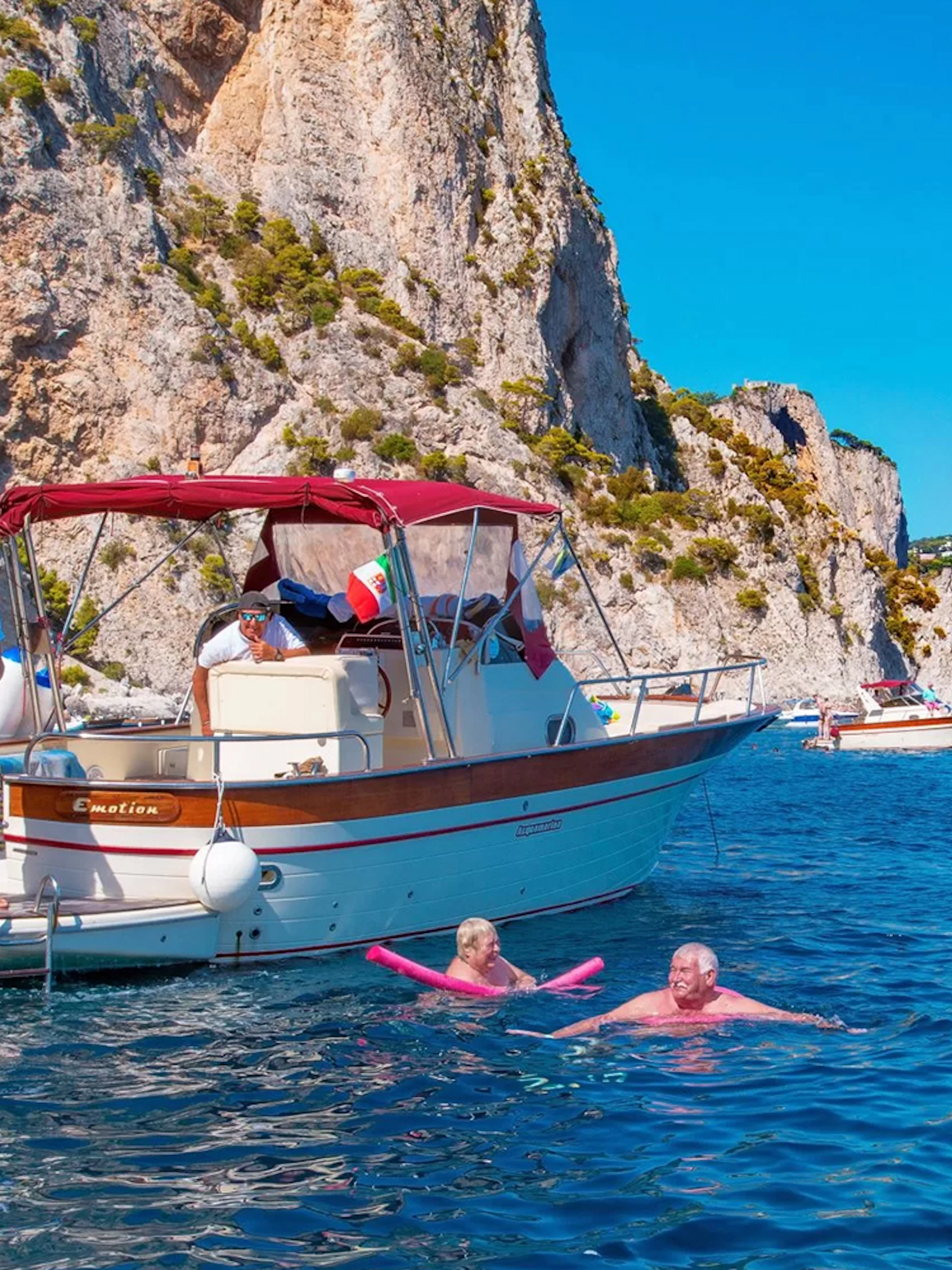 Boat tour with people swimming near cliffs in Capri, Italy.