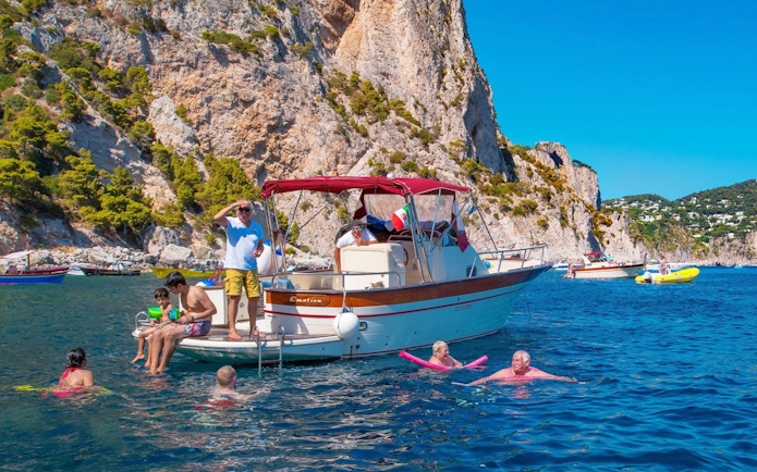 Boat tour with people swimming near cliffs in Capri, Italy.
