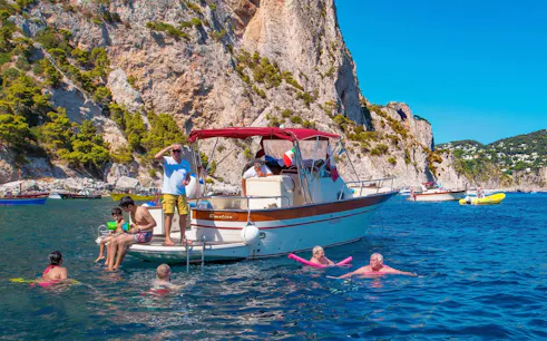 Boat tour with people swimming near cliffs in Capri, Italy.