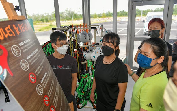 Visitors reading safety rules at Discovery Park, Gamuda Cove, with helmets and harnesses in the background.