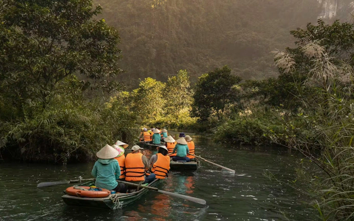 Visitors rowing boats through lush greenery at Trang An Landscape Complex, Vietnam.
