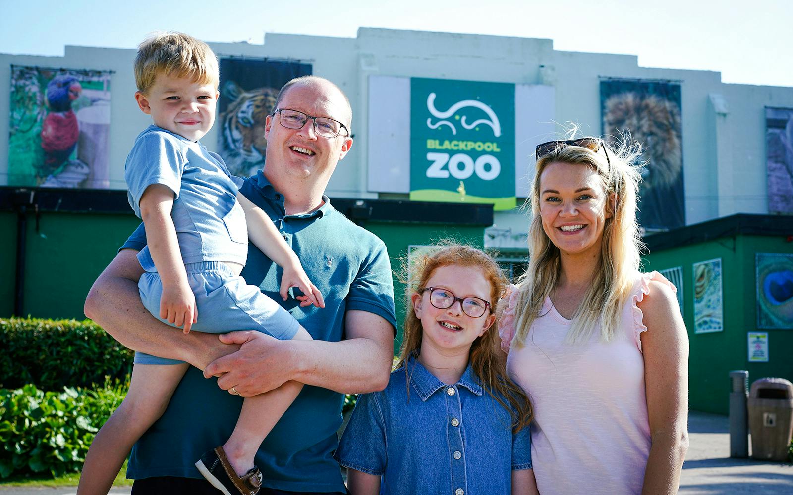 Family visiting Blackpool Zoo entrance with animal posters in background.