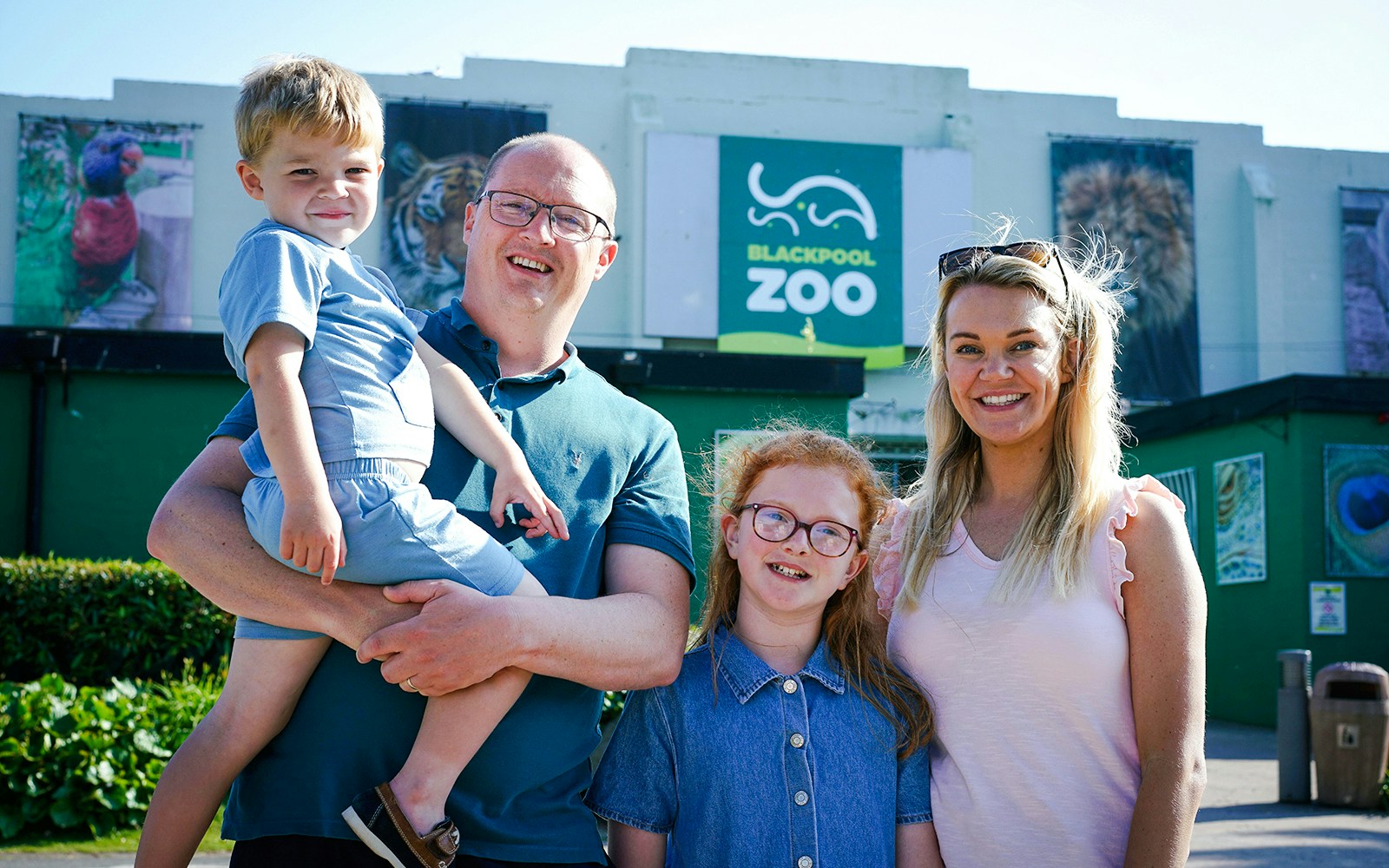 Family visiting Blackpool Zoo entrance with animal posters in background.