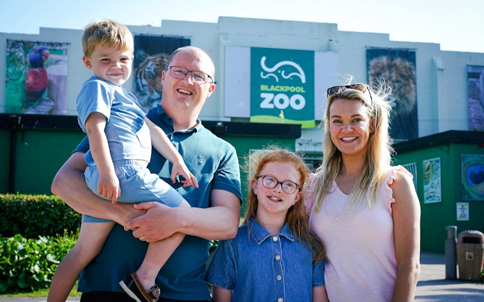 Family visiting Blackpool Zoo entrance with animal posters in background.