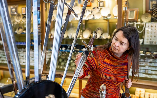 Woman examining swords in a Toledo shop during the Toledo Express Tour from Madrid.