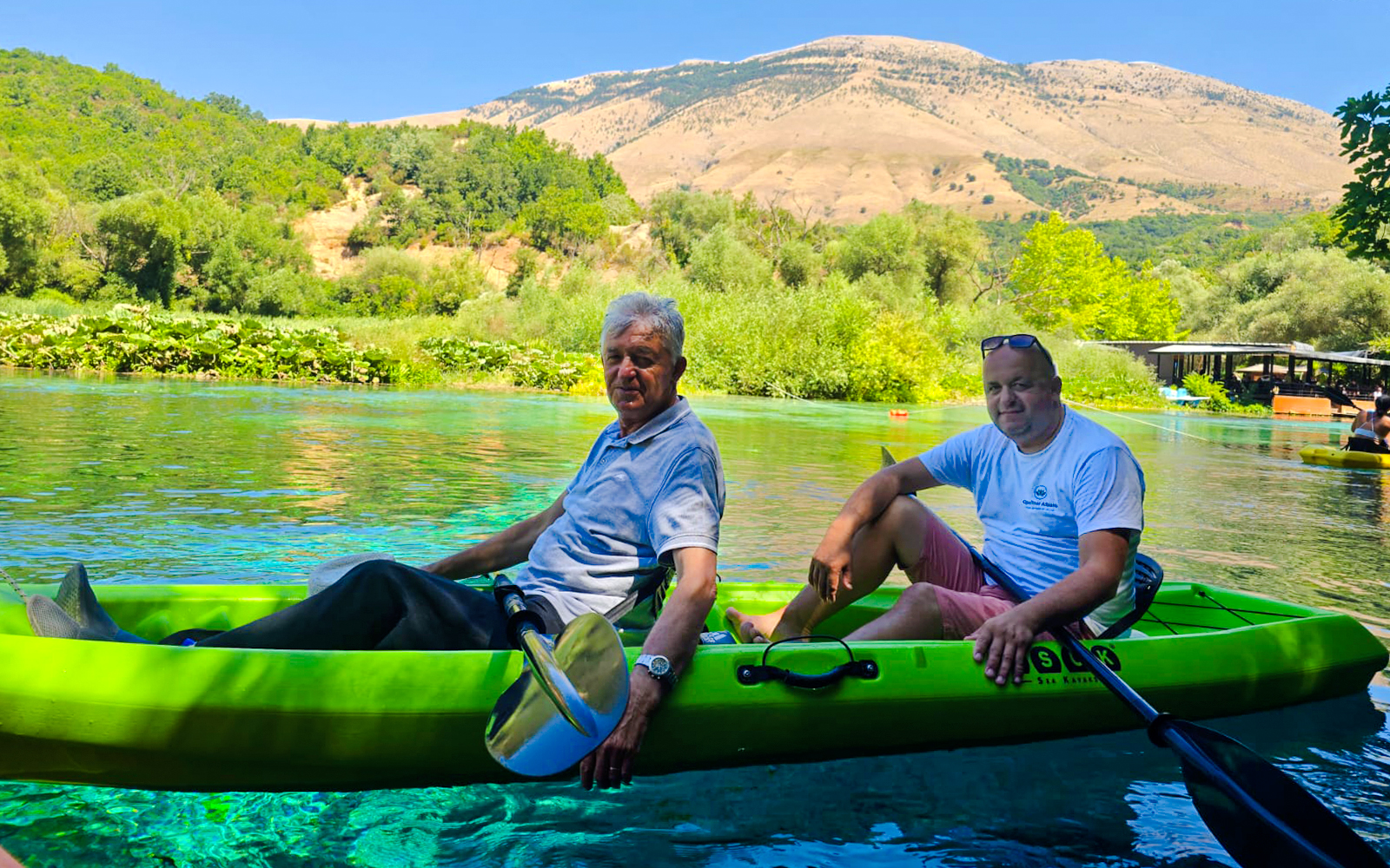 Guests kayaking on clear waters at The Blue Eye, Albania, with lush greenery and mountains in the background.