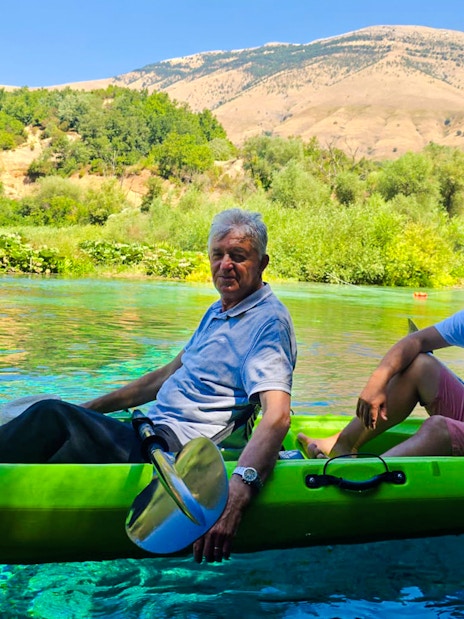 Guests kayaking on clear waters at The Blue Eye, Albania, with lush greenery and mountains in the background.