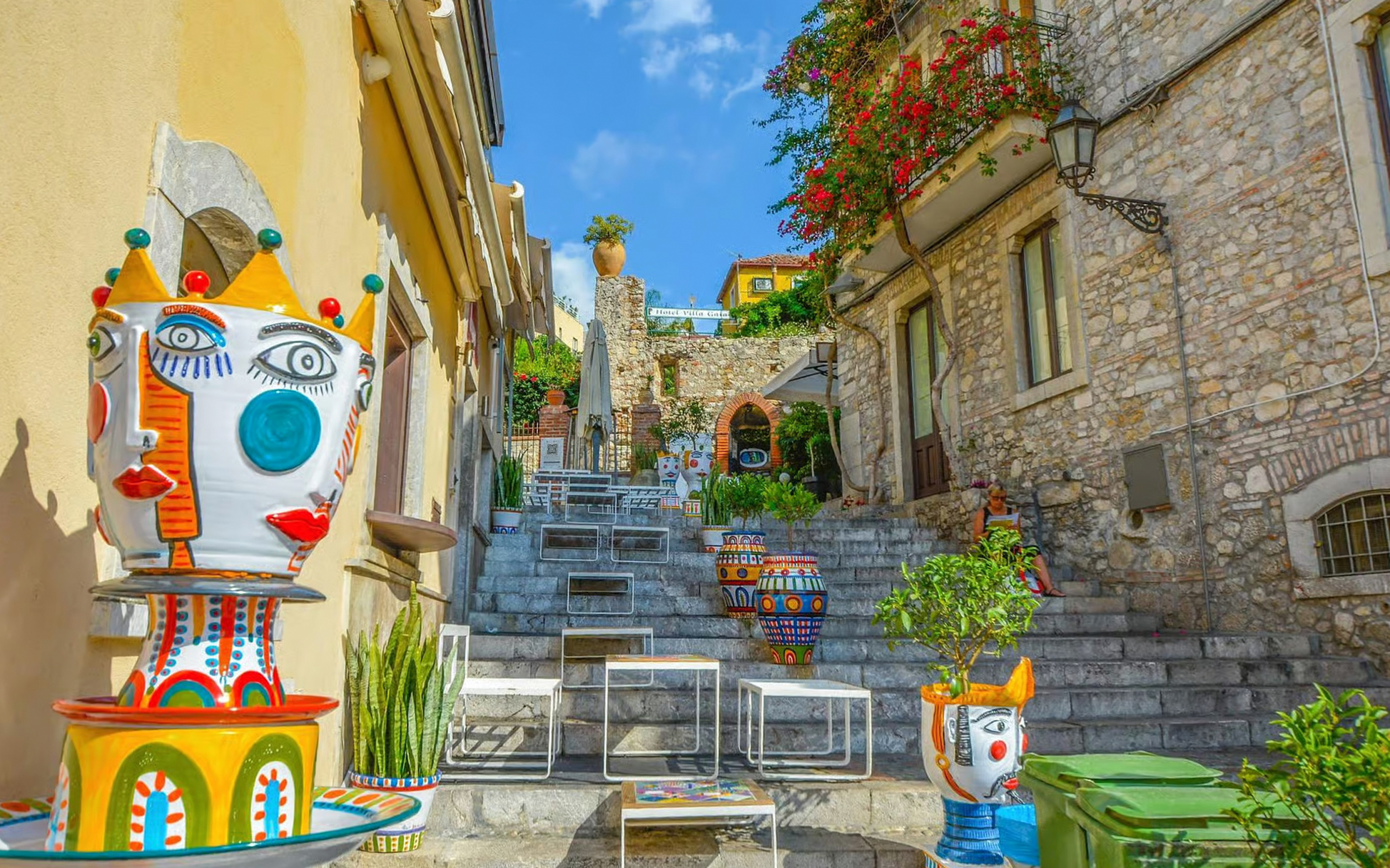 Colorful ceramic pots in a narrow alleyway in Taormina with stone steps and vibrant plants.