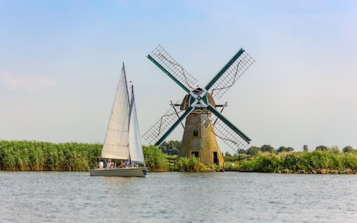 Sailboat near a traditional Dutch windmill on a countryside canal.