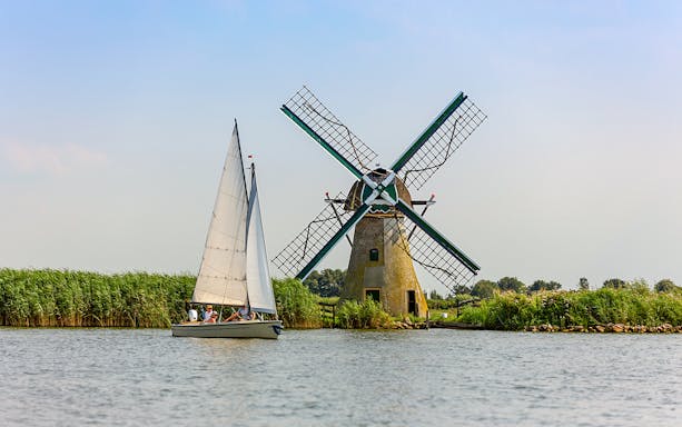 Sailboat near a traditional Dutch windmill on a countryside canal.