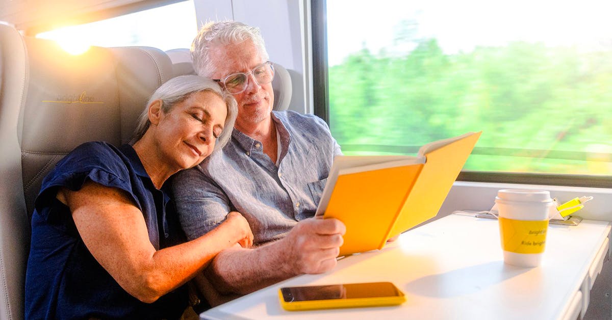 Couple relaxing on Brightline train from Miami to Orlando, reading and enjoying the journey.