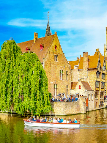 Canal cruise boat passing historic buildings in old town Brugge.