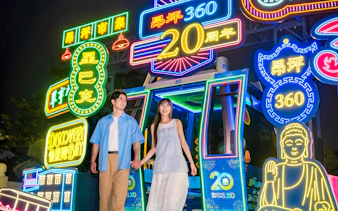 Couple holding hands in front of neon lights at Ngong Ping 360 cable car, Lantau Island.