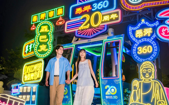 Couple holding hands in front of neon lights at Ngong Ping 360 cable car, Lantau Island.