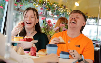 Guests enjoying pastries and sandwiches on a vintage tea tour bus decorated with flowers.