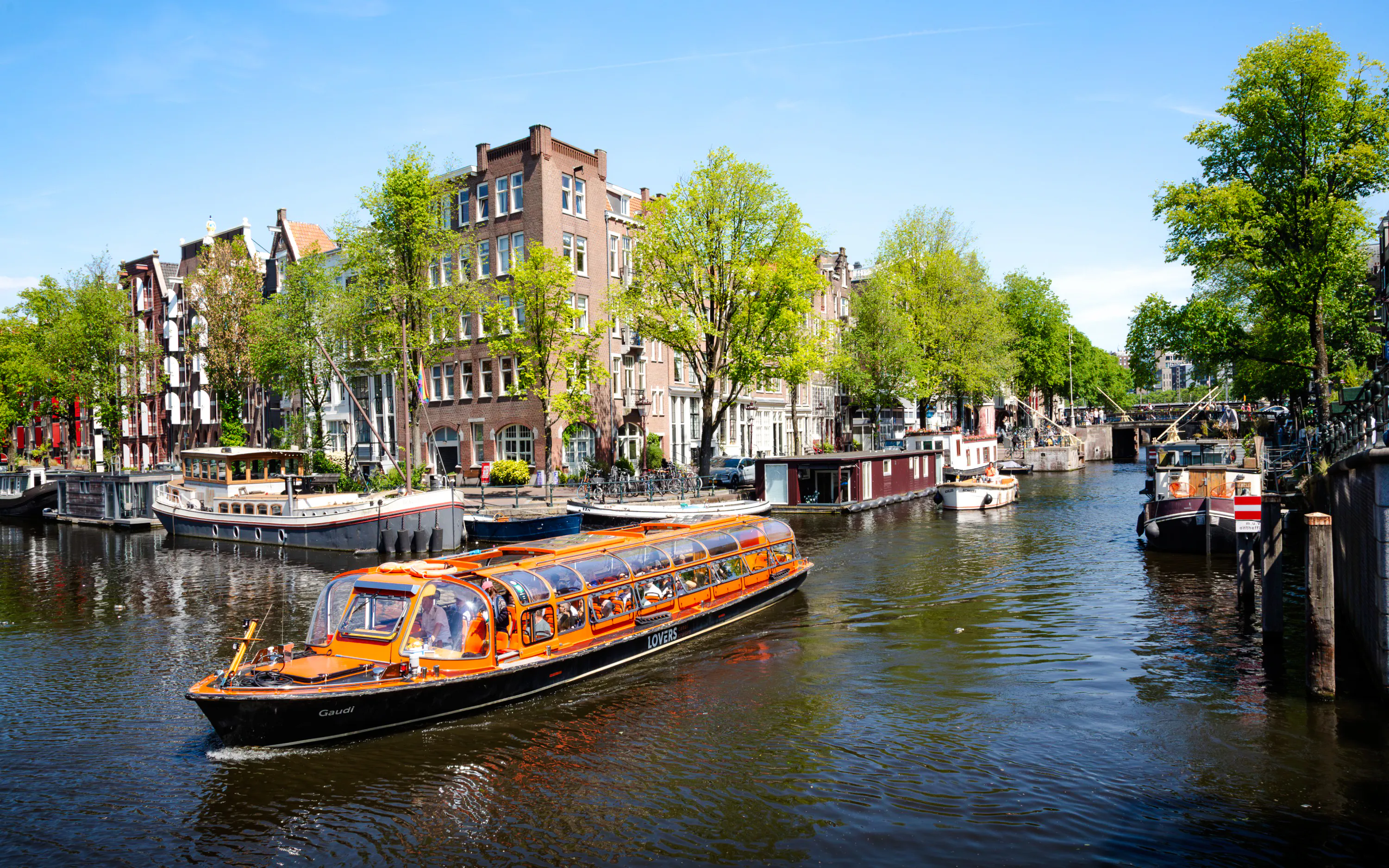 Canal cruise boat on Amsterdam canal with historic buildings and houseboats.