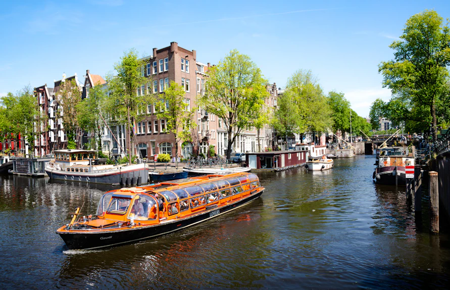 Canal cruise boat on Amsterdam canal with historic buildings and houseboats.