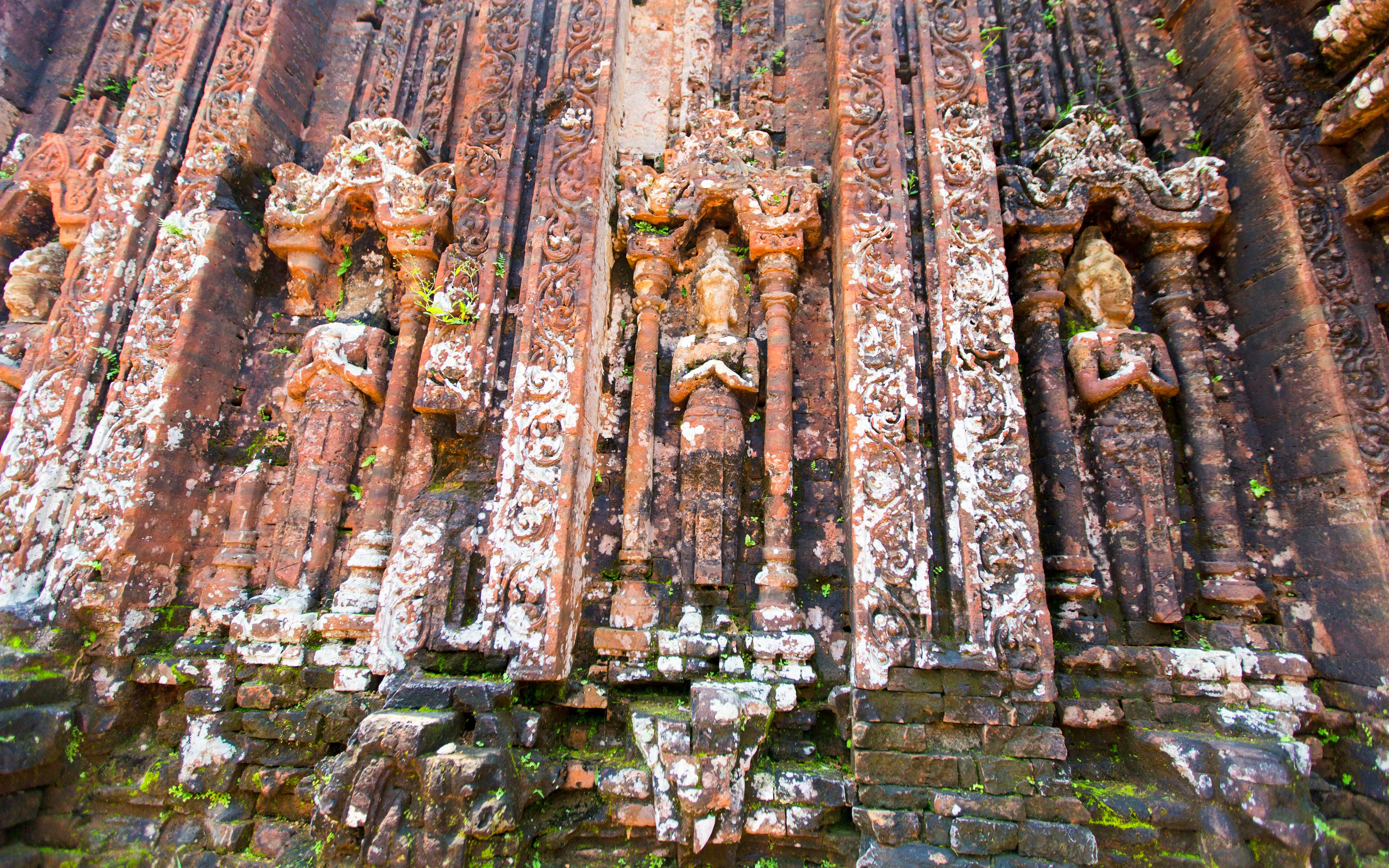Intricate sandstone relief carvings on ancient brick walls at Mỹ Sơn Sanctuary, Quảng Nam, Vietnam.