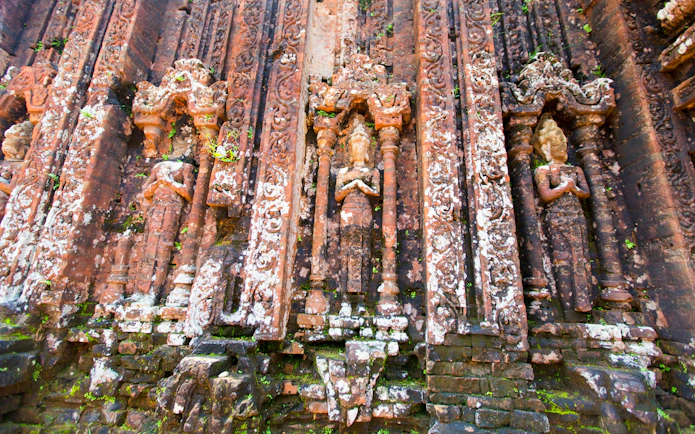 Intricate sandstone relief carvings on ancient brick walls at Mỹ Sơn Sanctuary, Quảng Nam, Vietnam.