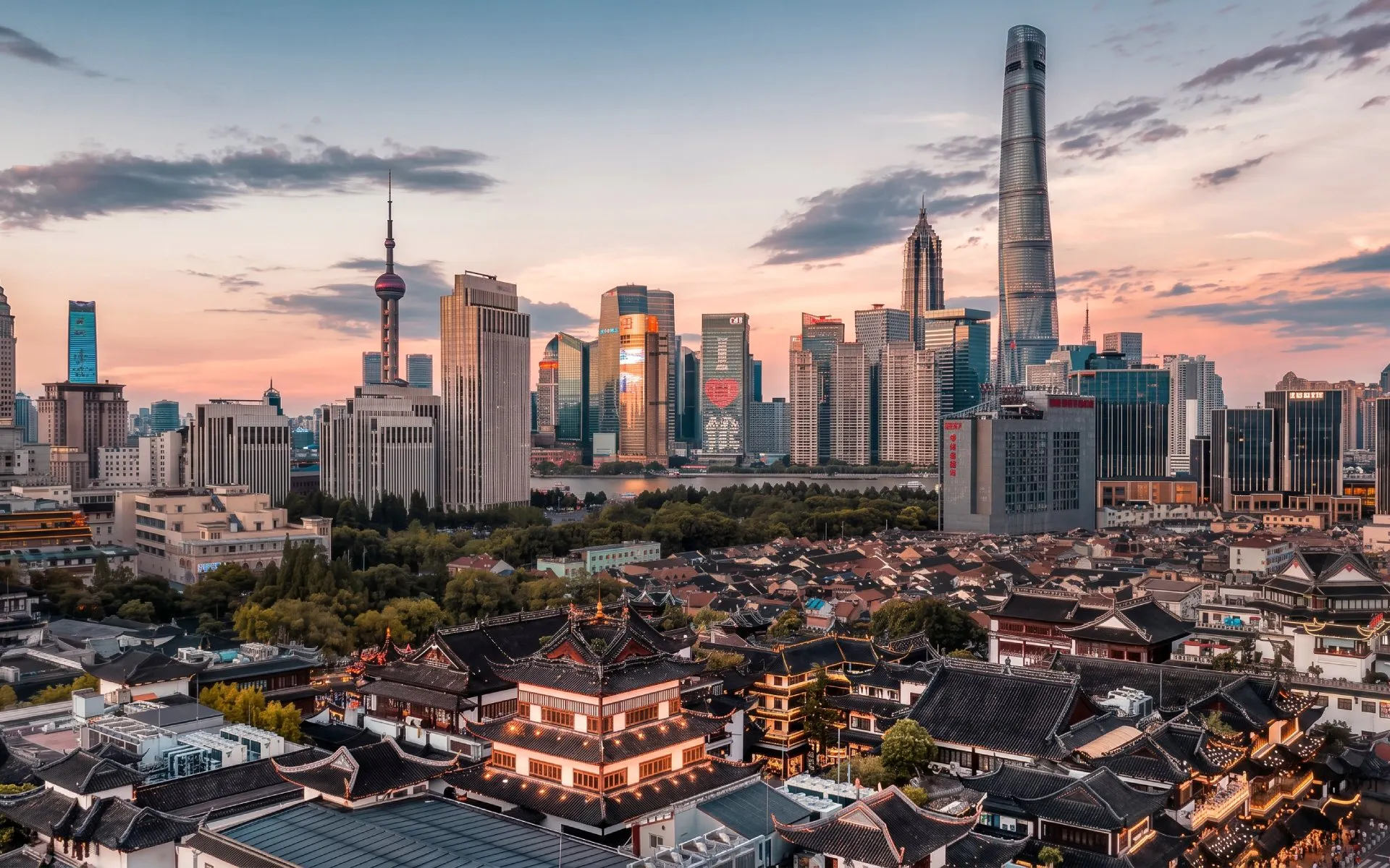Yu Garden with Shanghai skyline at sunset, featuring modern skyscrapers and traditional architecture.