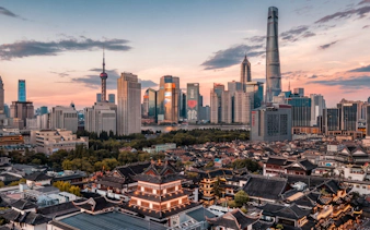 Yu Garden with Shanghai skyline at sunset, featuring modern skyscrapers and traditional architecture.