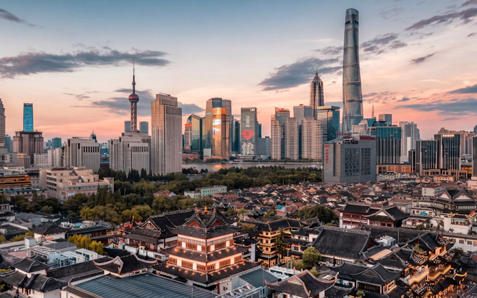 Yu Garden with Shanghai skyline at sunset, featuring modern skyscrapers and traditional architecture.