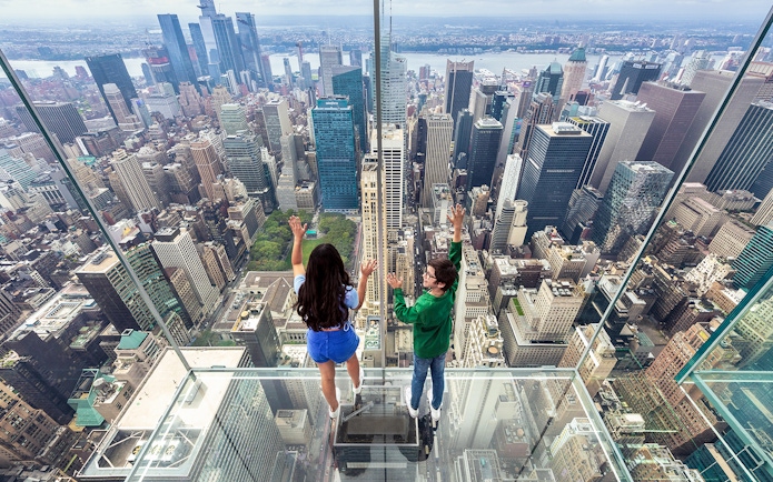 Tourists on glass floor at SUMMIT One Vanderbilt overlooking New York City skyline.