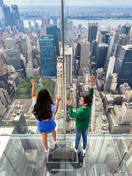 Tourists on glass floor at SUMMIT One Vanderbilt overlooking New York City skyline.