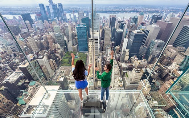 Tourists on glass floor at SUMMIT One Vanderbilt overlooking New York City skyline.