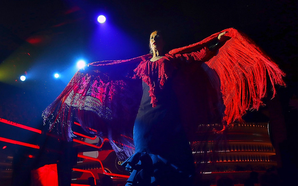 Flamenco dancer performing under stage lights with red shawl, Spain.