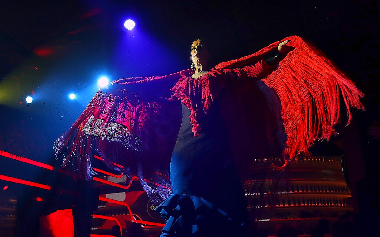 Flamenco dancer performing under stage lights with red shawl, Spain.