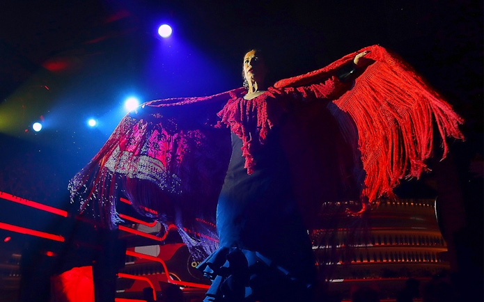 Flamenco dancer performing under stage lights with red shawl, Spain.