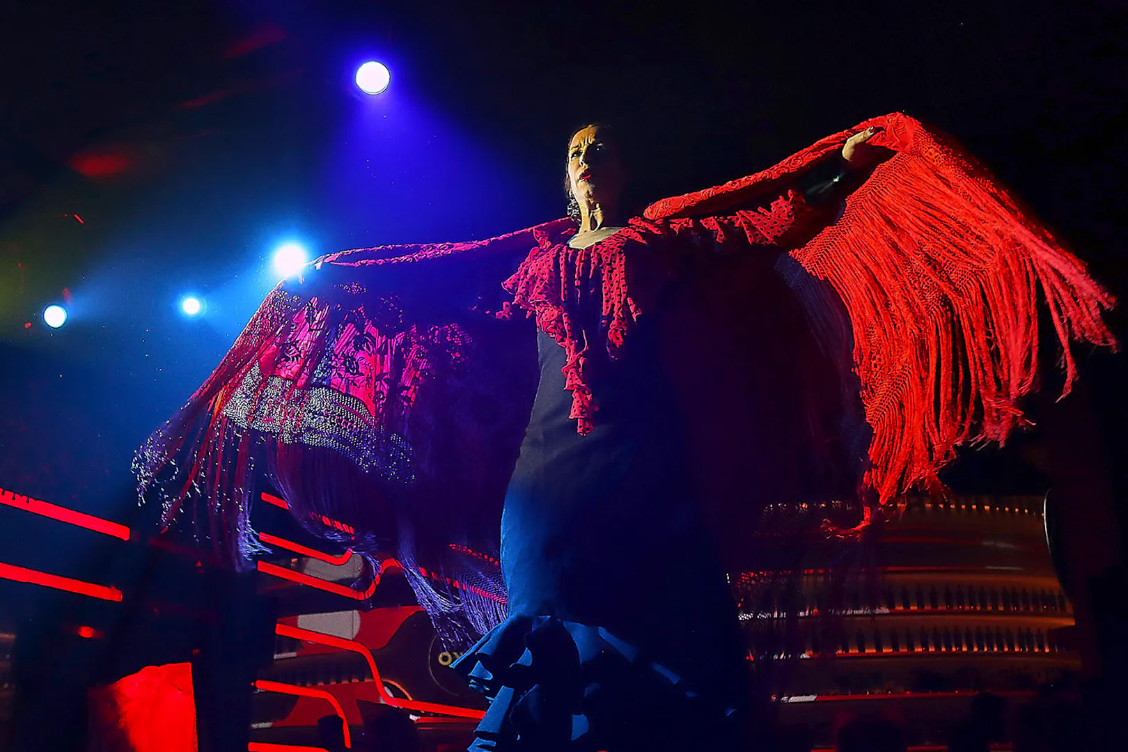 Flamenco dancer performing under stage lights with red shawl, Spain.